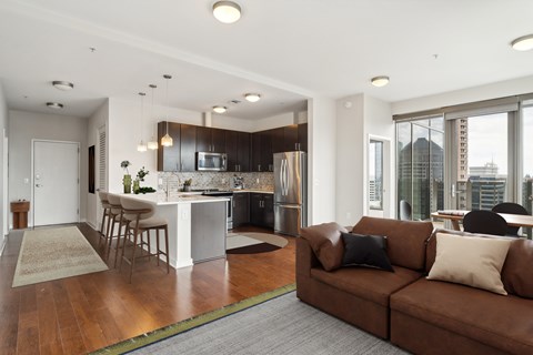 A modern living room with a brown couch and a kitchen in the background.